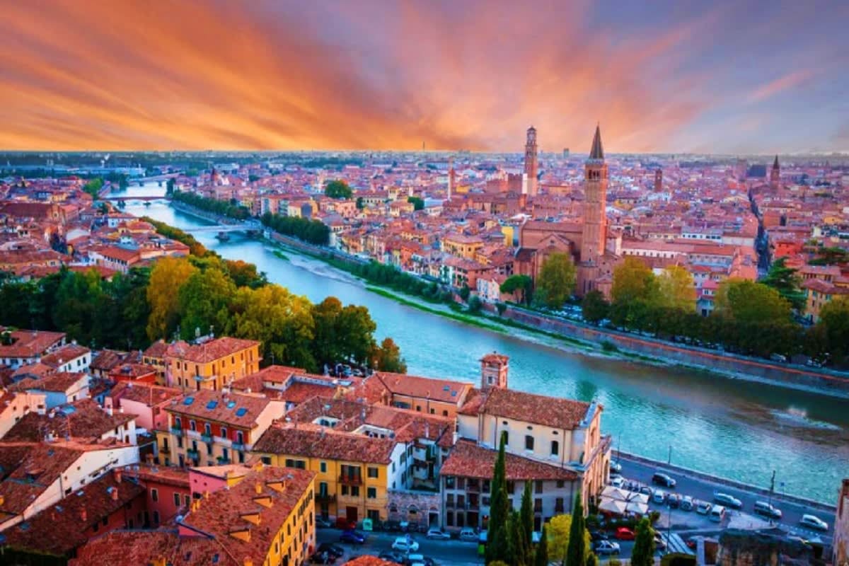 Aerial sunset view of Verona, Italy with Adige River, historic buildings with terracotta roofs, and church towers at dusk