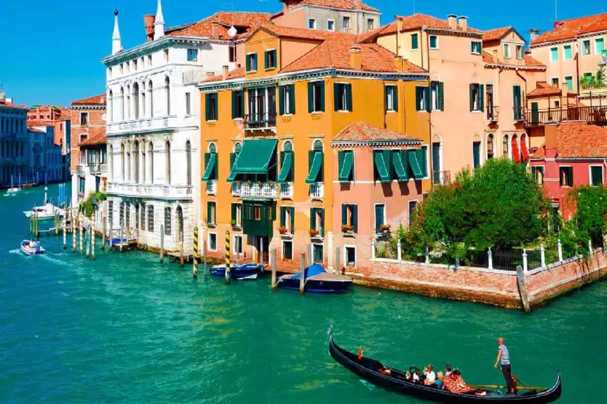 Gondola on turquoise canal with colorful historic buildings and white palazzo in Venice, Italy