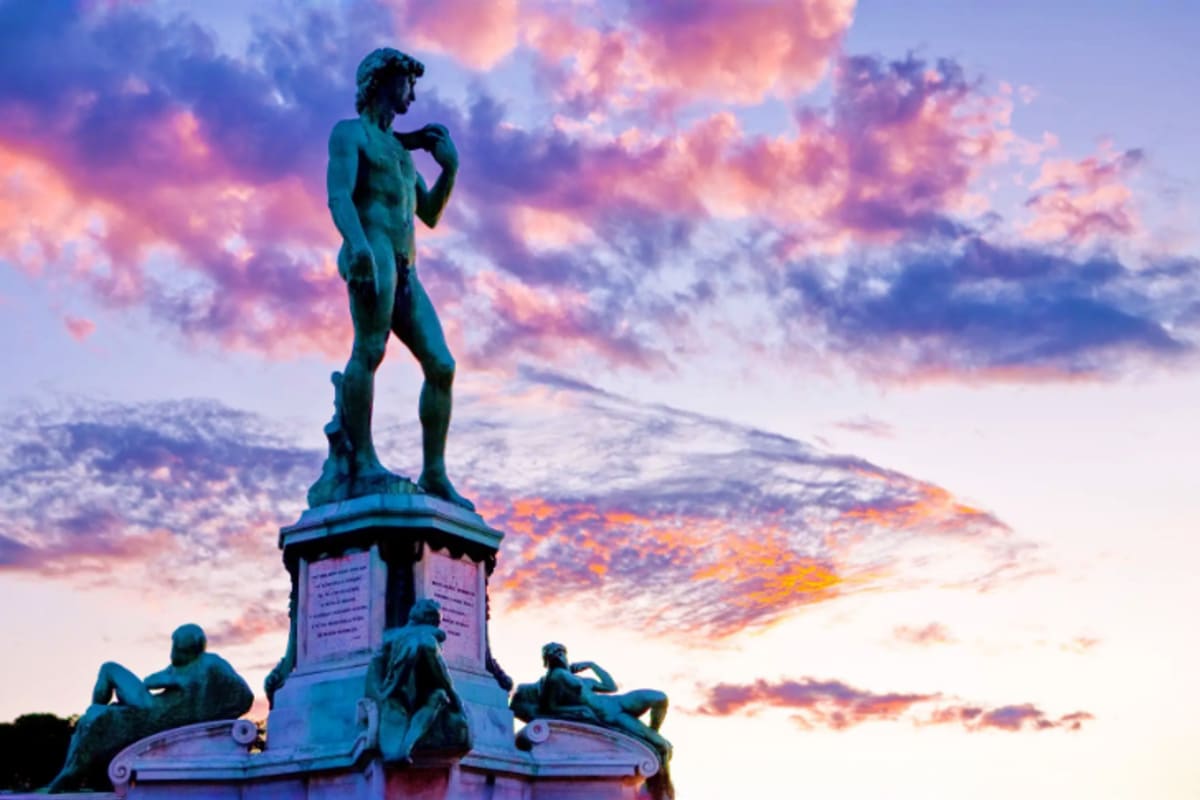 Central Europe Romance Tour With Prague to Venice for Couples Bronze statue of male figure on pedestal with allegorical sculptures at base against dramatic sunset sky with pink and purple