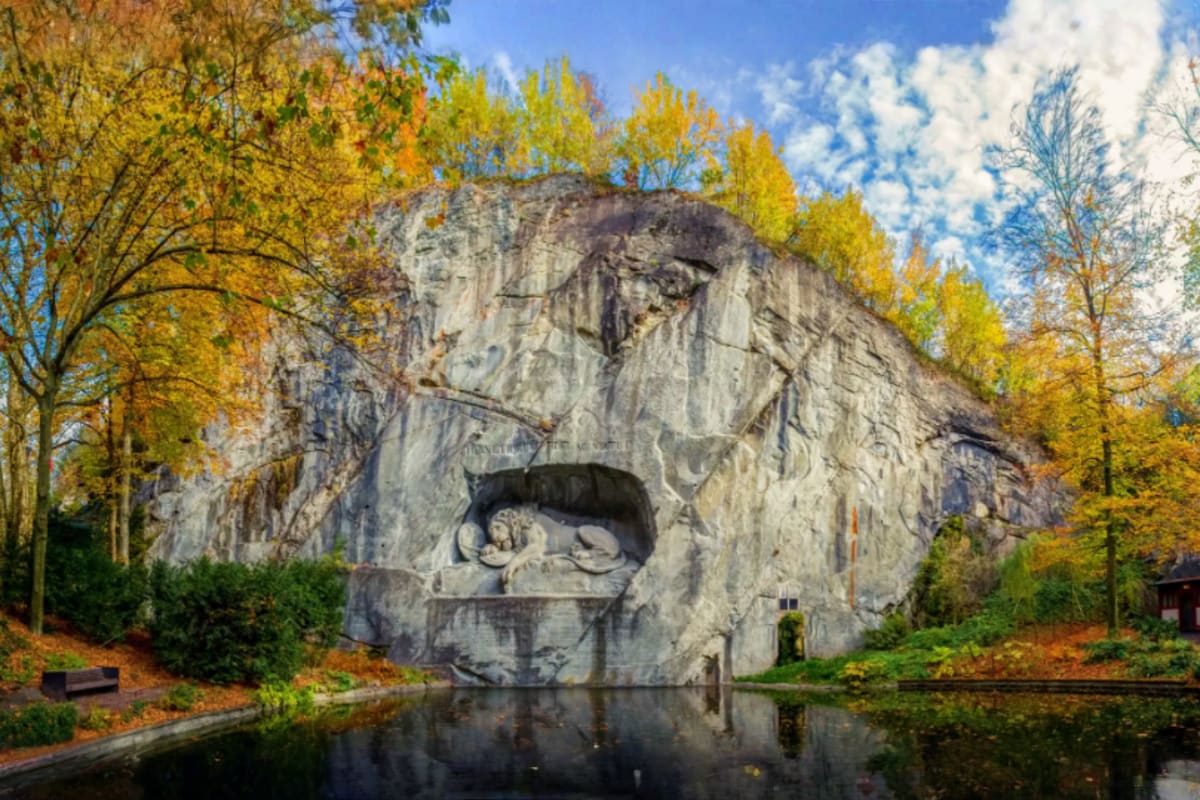 Central Europe Romance Tour With Prague to Venice for Couples Lion Monument carved into rock face overlooking still water with autumn trees in Lucerne, Switzerland