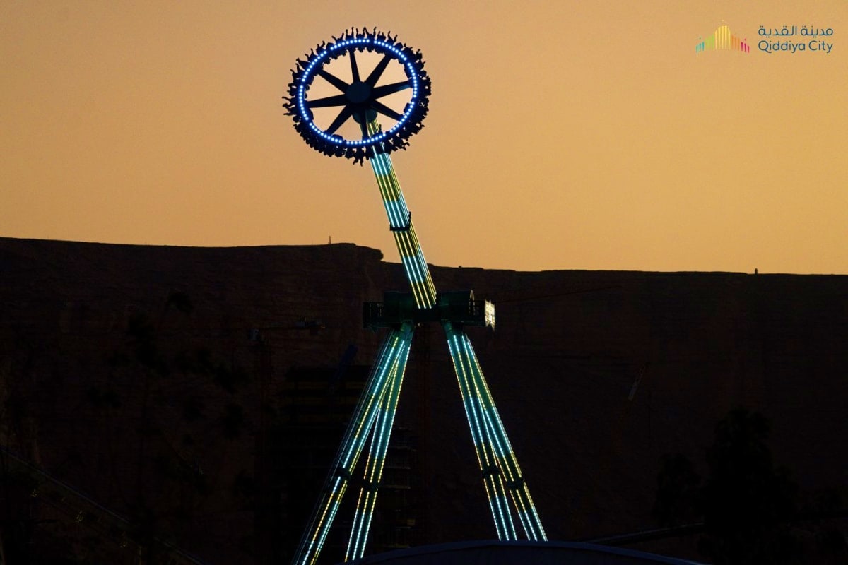 Illuminated blue ferris wheel with glowing support cables at dusk in Qiddiya City entertainment destination