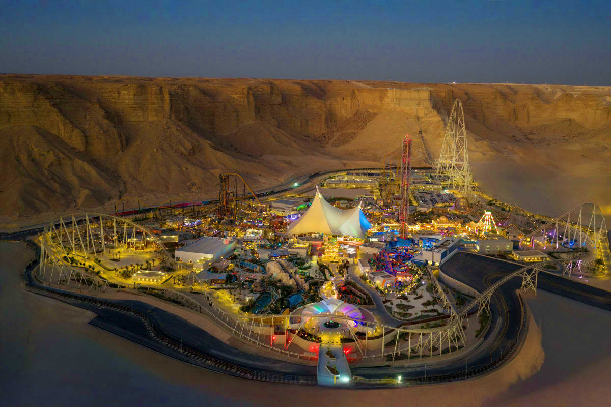 Aerial view of illuminated amusement park with roller coasters and rides nestled in desert cliffs at dusk in Riyadh