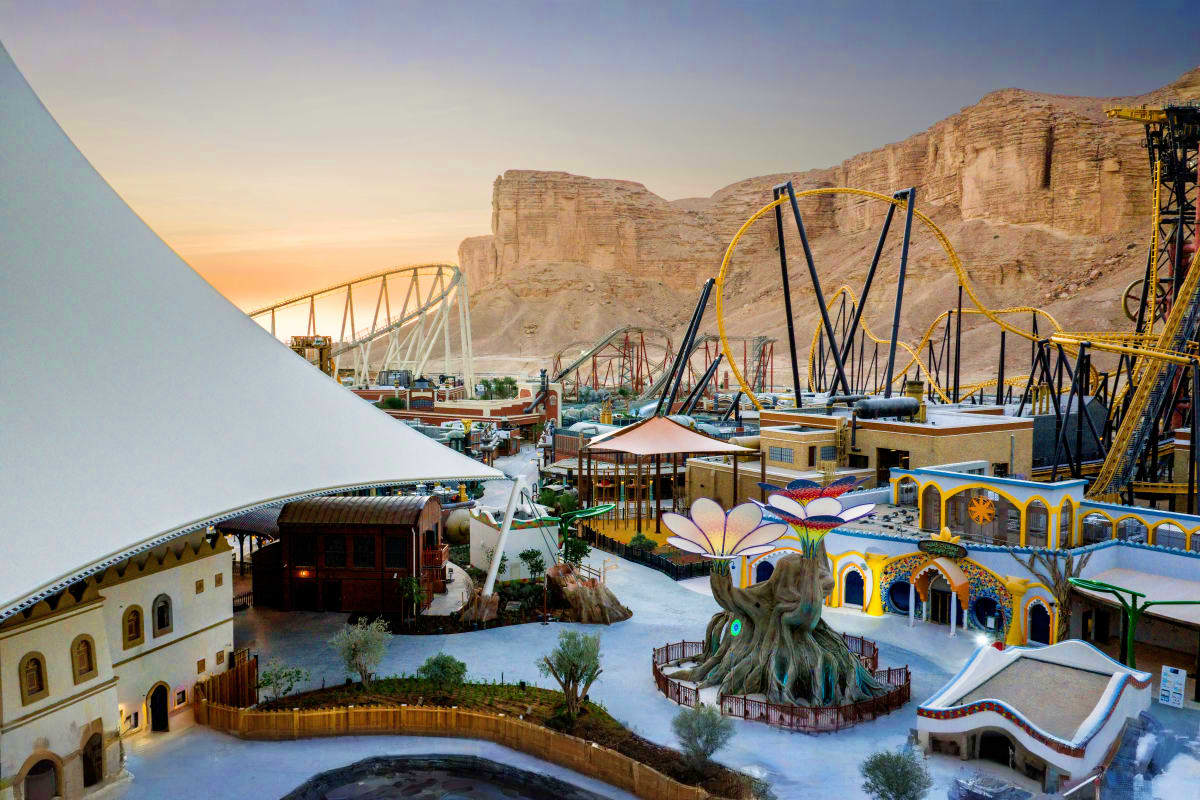 Aerial view of theme park with roller coasters and colorful buildings against desert cliffs at sunset in Riyadh