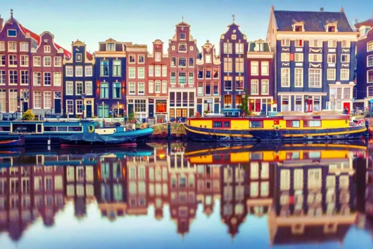 Colorful historic buildings lining Amsterdam canal with traditional boats and perfect water reflections