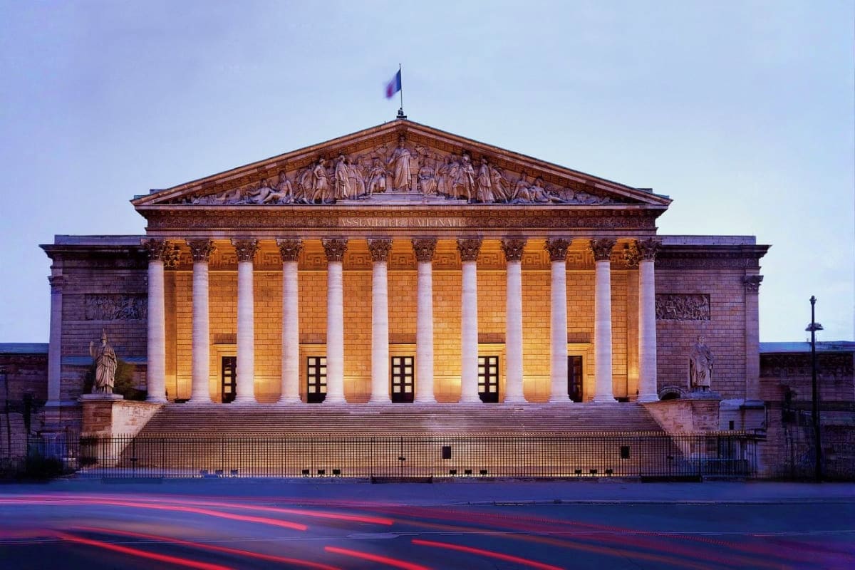French National Assembly building illuminated at twilight with classical columns and pediment sculpture in Paris