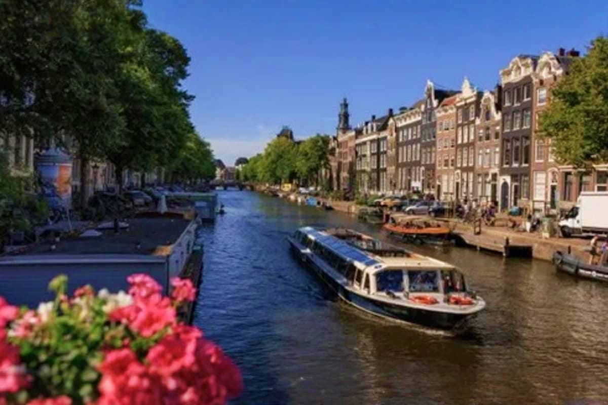 Canal boat tour passing historic brick buildings and pink flowers in Amsterdam waterway