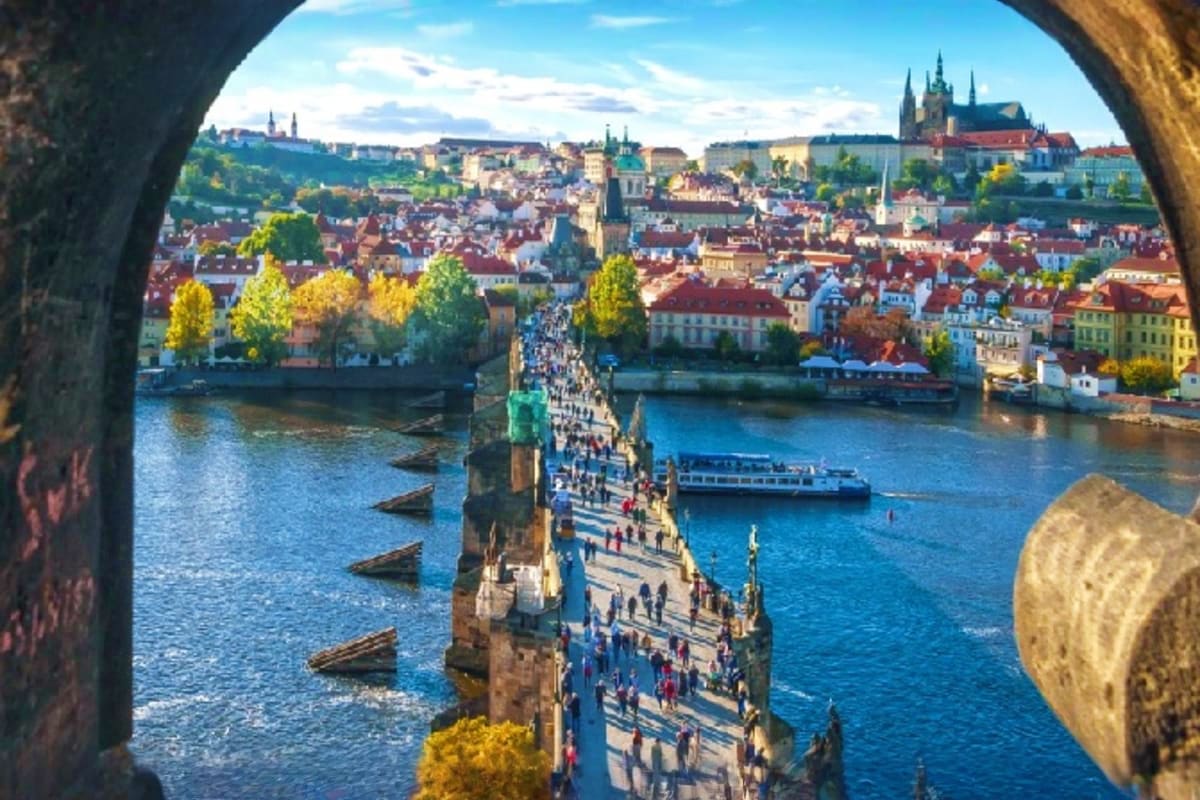 View through stone arch of Charles Bridge spanning Vltava River with Prague castle and old town skyline in background