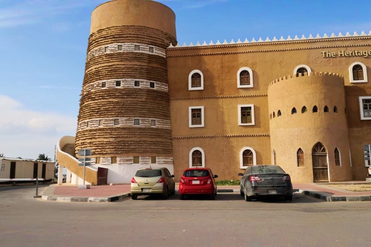Historic Islamic architecture with cylindrical spiral tower and tan fortress-style building with white arched windows in Damm