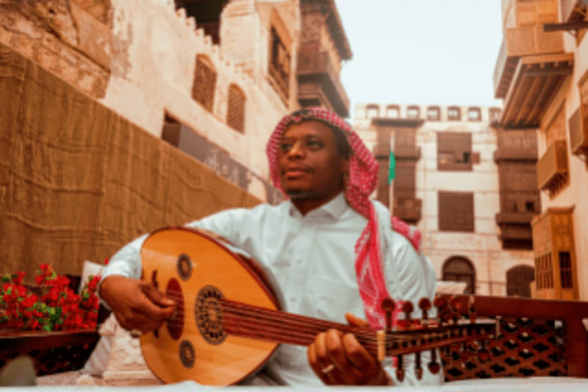 Man in traditional Arab dress playing oud in historic courtyard with traditional architecture and red flowers