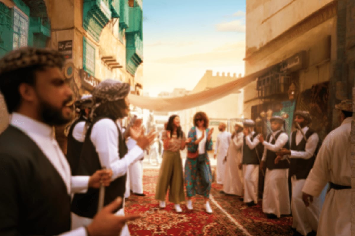 Crowd of people in traditional clothing gathering in a narrow Middle Eastern street with historic architecture and fortress w