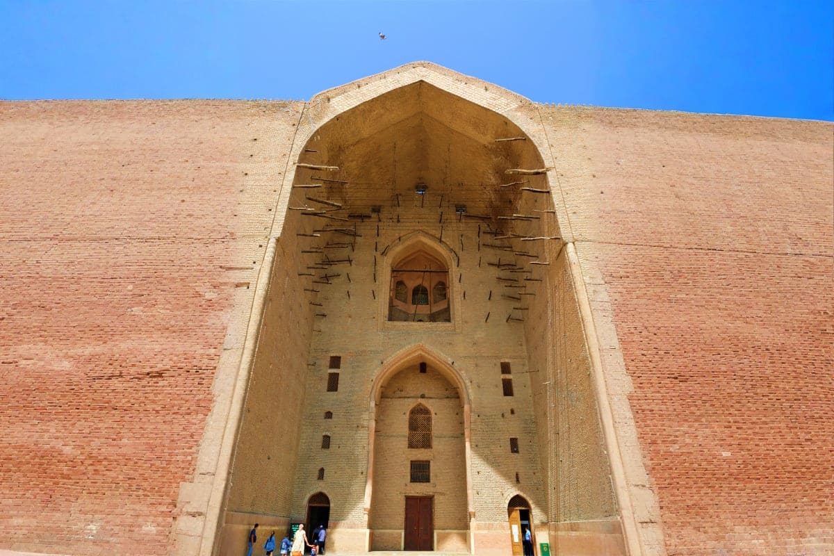 Historic brick mausoleum with pointed arch entrance and decorative geometric patterns, tourists visiting cultural landmark in