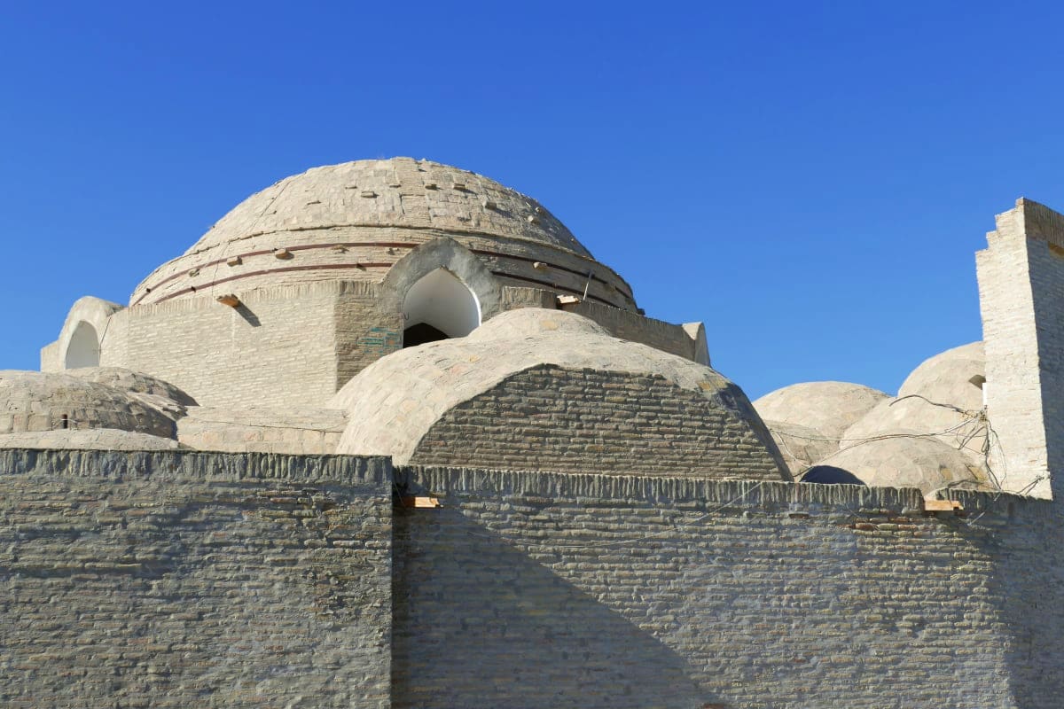 Historic stone building with domed roof and ornate Islamic architecture against clear blue sky in Uzbekistan