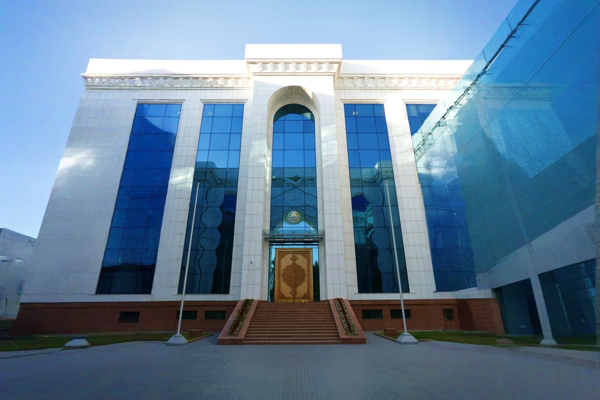 Modern white building with blue glass windows and ornate arches, featuring decorative bronze doors and brick base with grand 