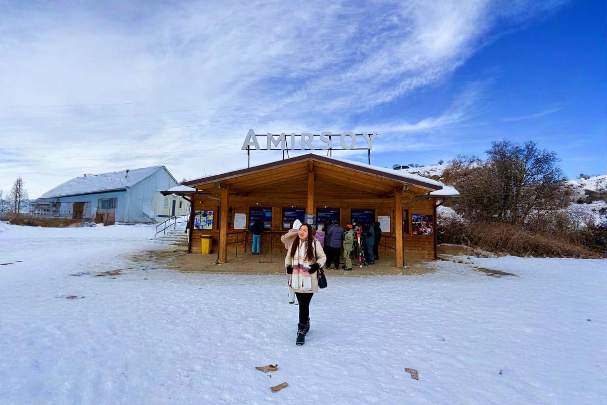 Woman ice skating on frozen lake at Amirsoy winter resort with wooden station building and snow-covered landscape in Uzbekist
