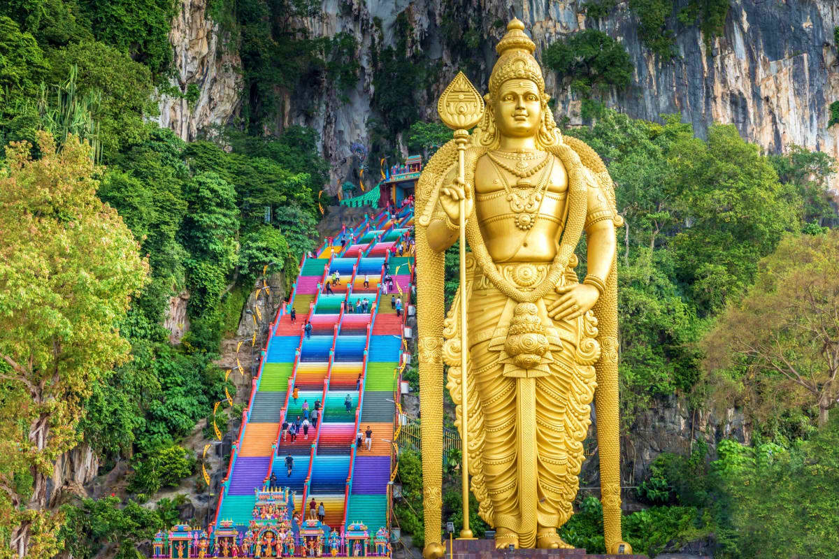 Tall golden Hindu statue overlooking colorful rainbow staircase at Batu Caves temple in Kuala Lumpur, Malaysia