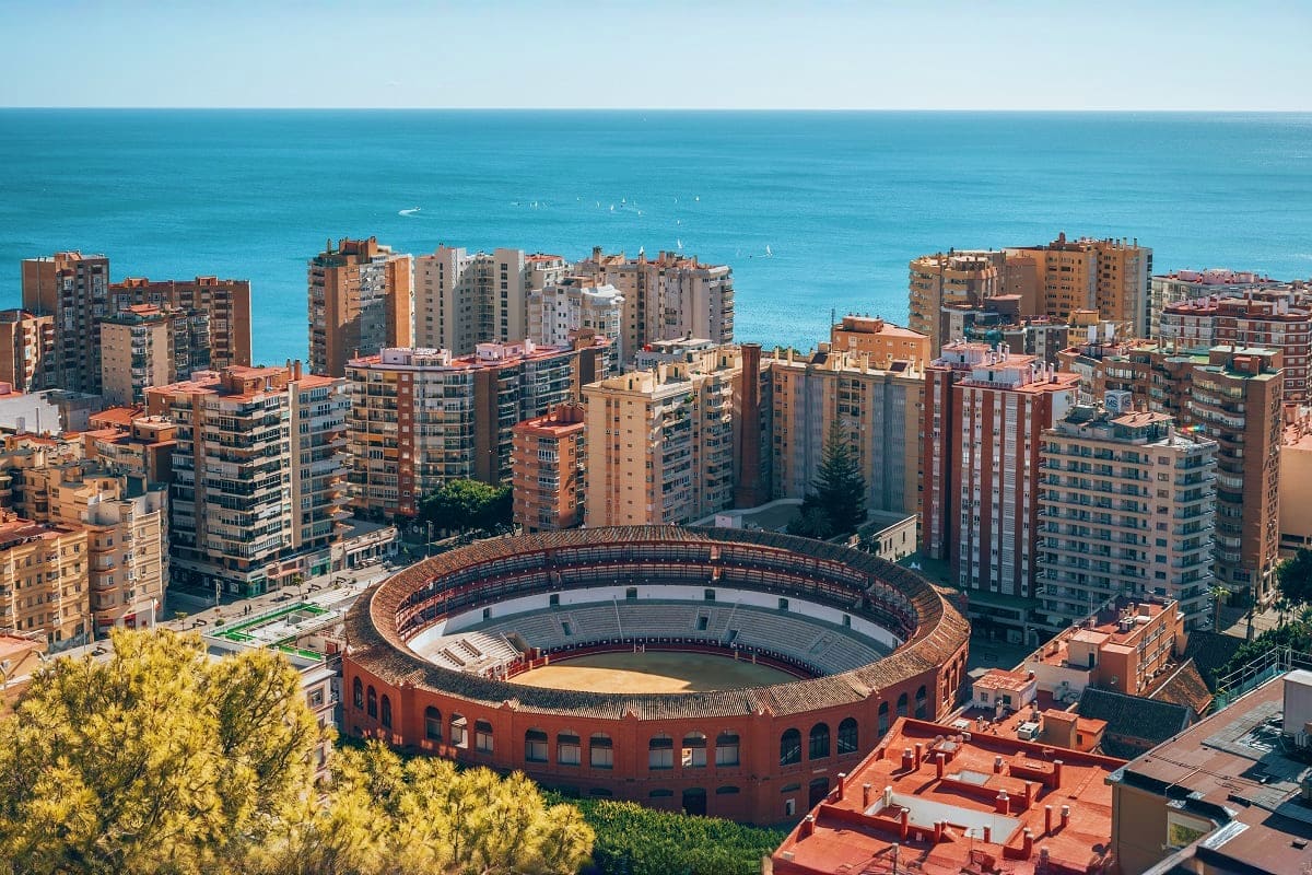 Aerial view of a historic bullring surrounded by Mediterranean coastal buildings and turquoise sea in Malaga, Spain