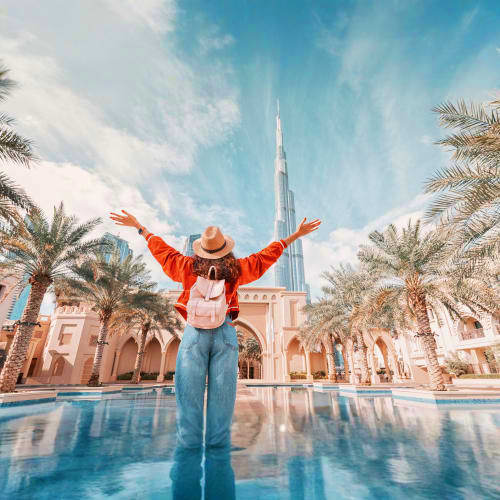 Woman with raised arms standing in reflecting pool in front of pink mosque and Burj Khalifa in Dubai