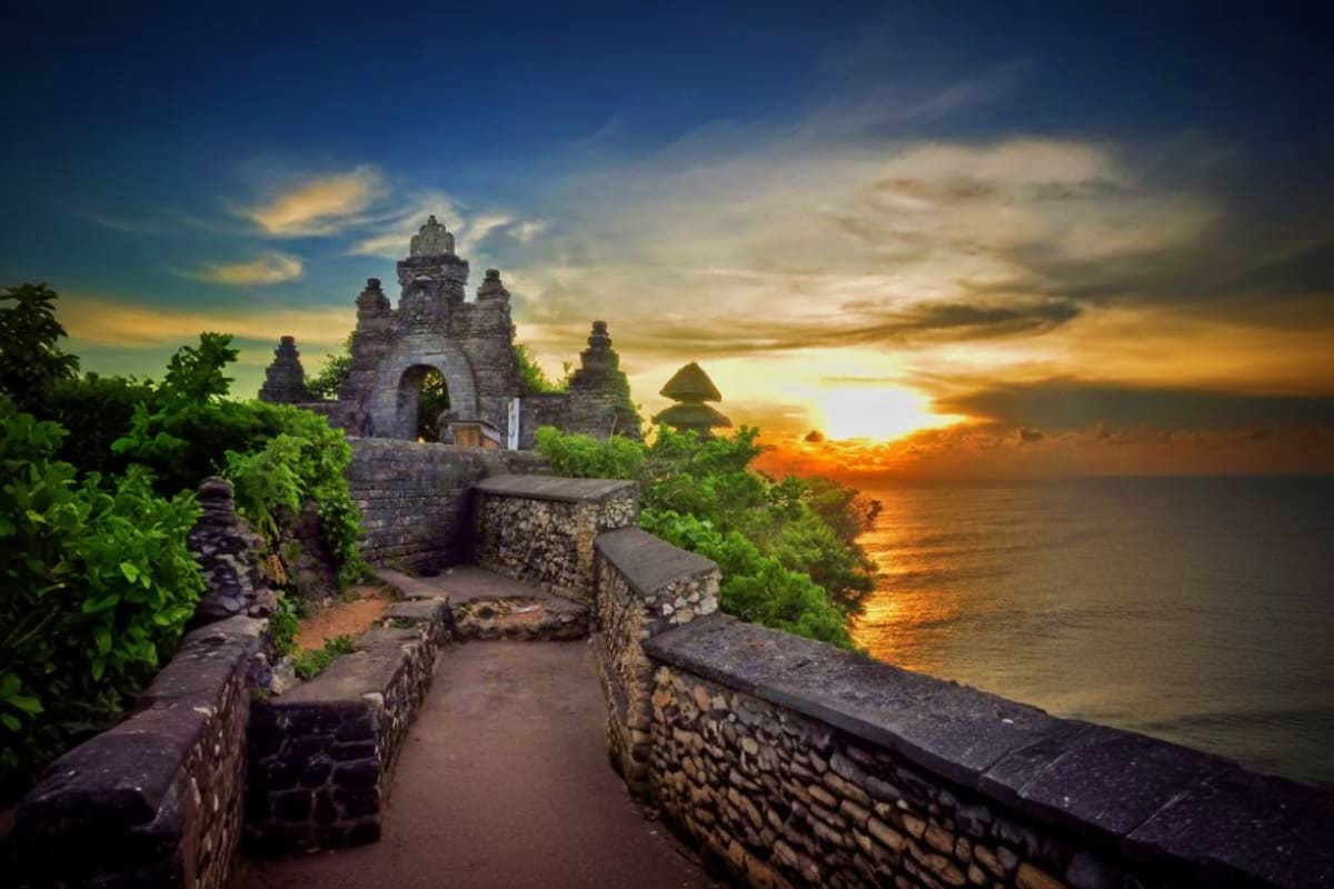 Ancient stone temple ruins with ornate architecture overlooking a golden sunset ocean view in Bali, Indonesia, surrounded by
