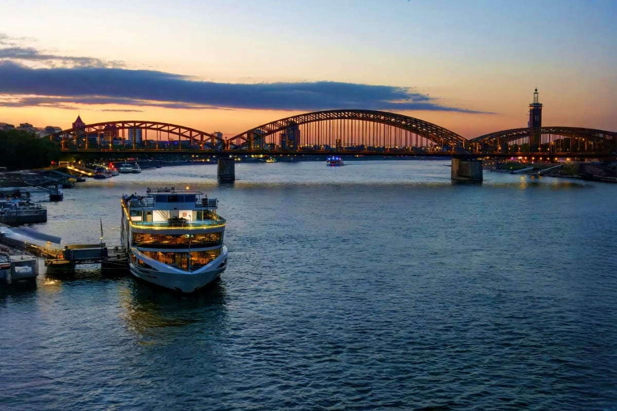 From Prague to Paris Illuminated riverboat on the Main River at sunset with the Iron Footbridge spanning across the water in Frankfurt, Germany