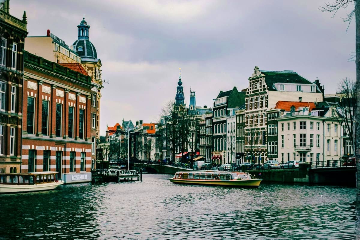 Tour boat on Amsterdam canal with historic architecture and green dome building along waterfront