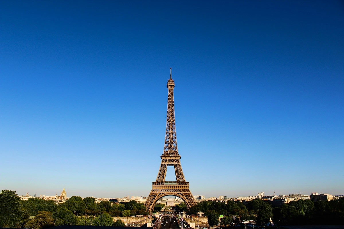 Eiffel Tower standing tall against clear blue sky with Paris cityscape and green trees in background