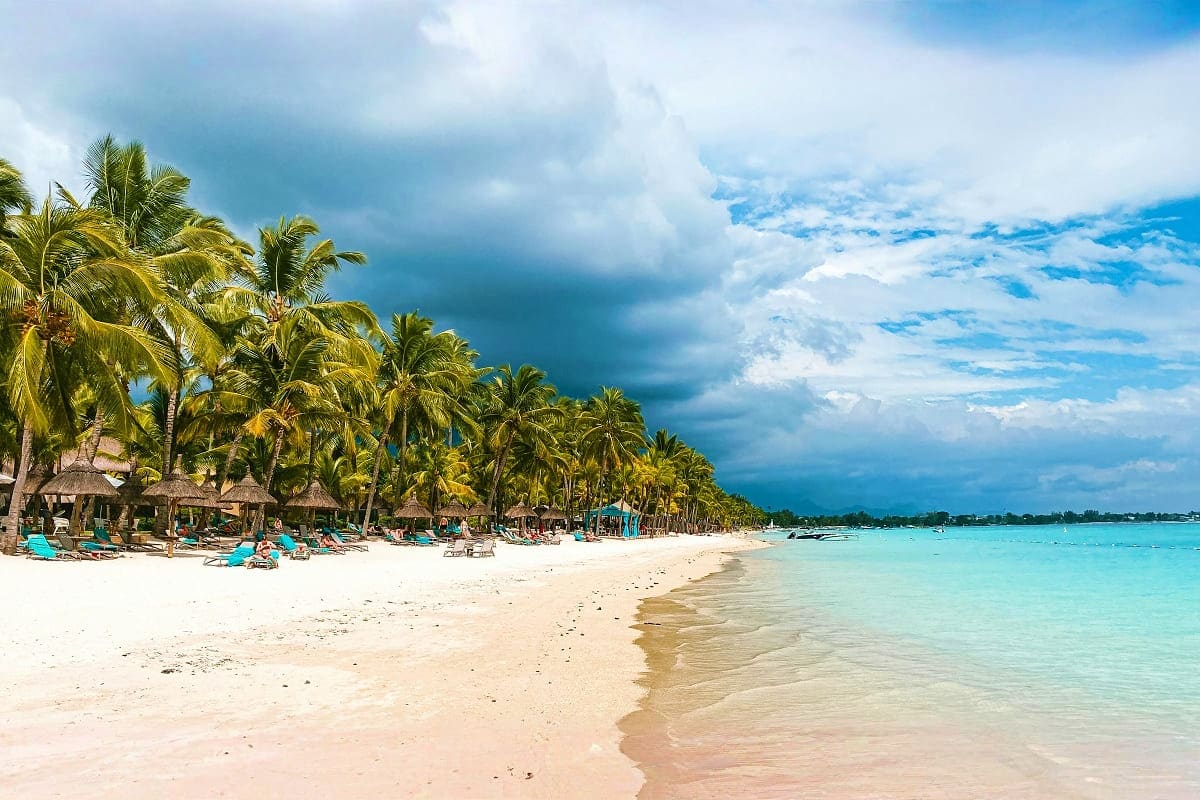 Incredible Mauritius Tropical beach in Mauritius with white sand, turquoise water, palm trees, thatched beach huts, and blue sky with clouds