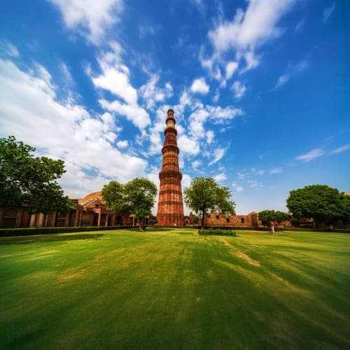 Qutb Minar ancient red sandstone tower surrounded by green lawn and historic structures under blue sky in Delhi