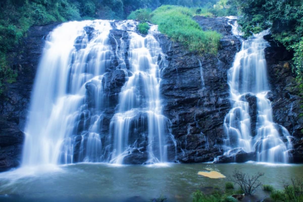 Natures Embrace Karnataka and Kerala Escape Multi-tiered waterfall cascading over dark rock formations into a turquoise pool, surrounded by lush green forest vegetation