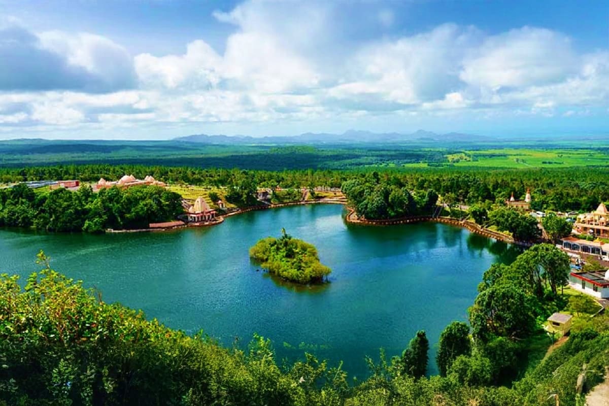 Aerial view of a serene turquoise lake surrounded by lush green forests, temples, and colonial architecture in Mauritius