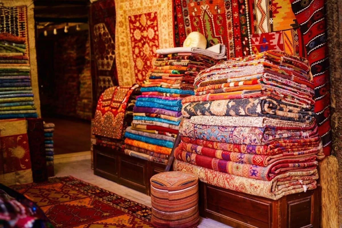 Traditional Turkish carpets and textiles stacked on wooden display in market shop with hanging rugs and woven patterns