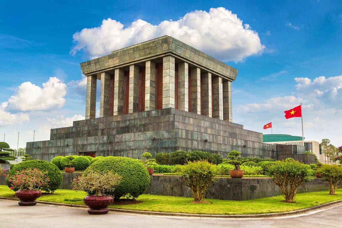 Vietnam Cultural Journey for Families Ho Chi Minh Mausoleum in Hanoi with Vietnamese flags, stone columns, manicured gardens, and blue sky with white clouds