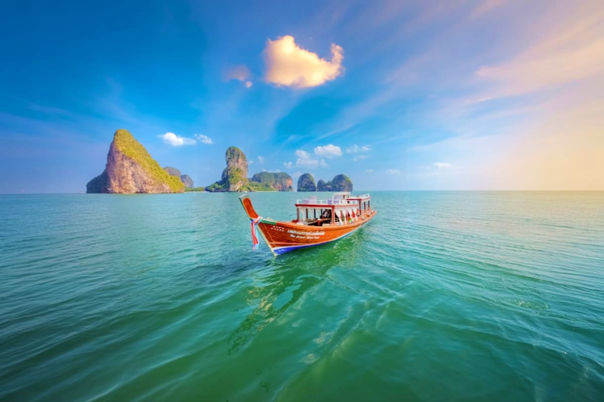04 Island Tour on Long Tail Boat Traditional red and white long tail boat in turquoise water with limestone karst islands in background under blue sky