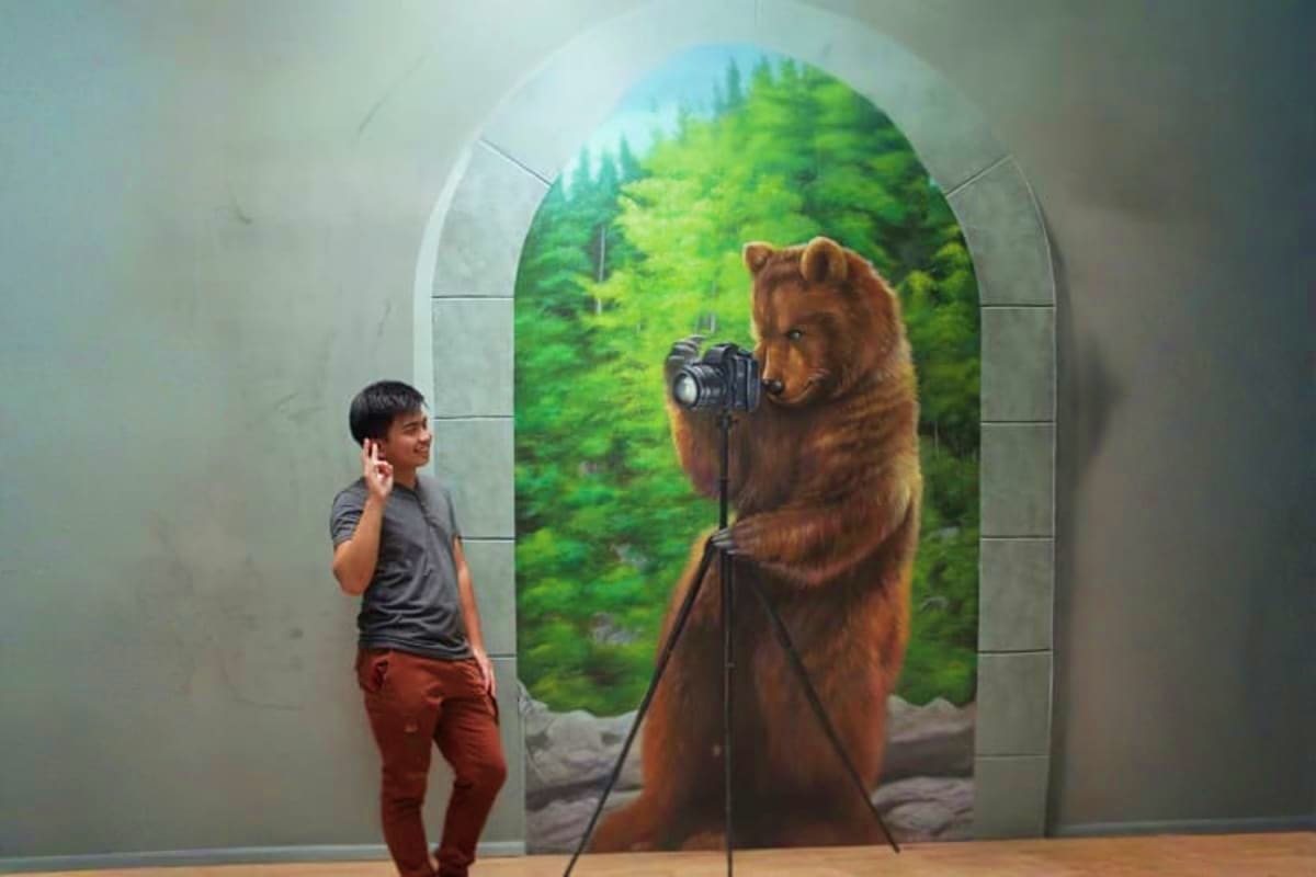 Child standing in front of 3D mural of brown bear holding camera with forest background at interactive museum exhibit