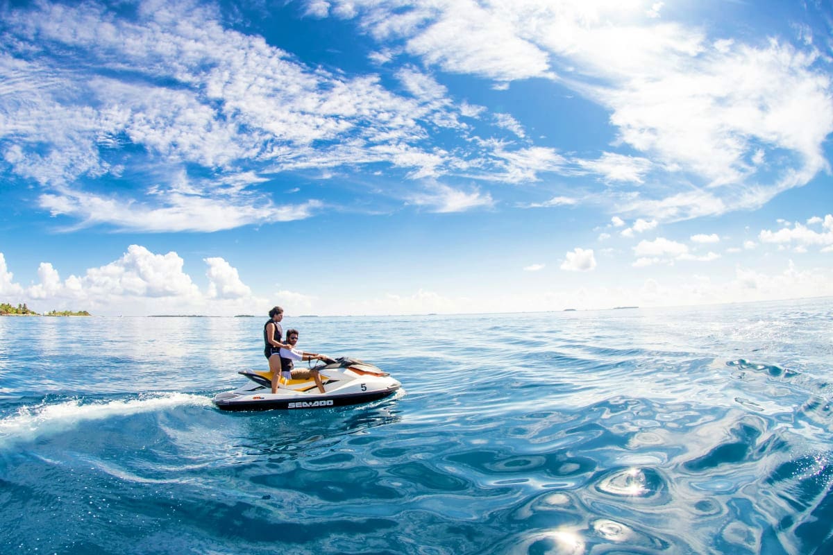 Jet ski Experience in Abu Dhabi Adult and child riding a jet ski in clear blue water with white clouds and distant islands in Abu Dhabi