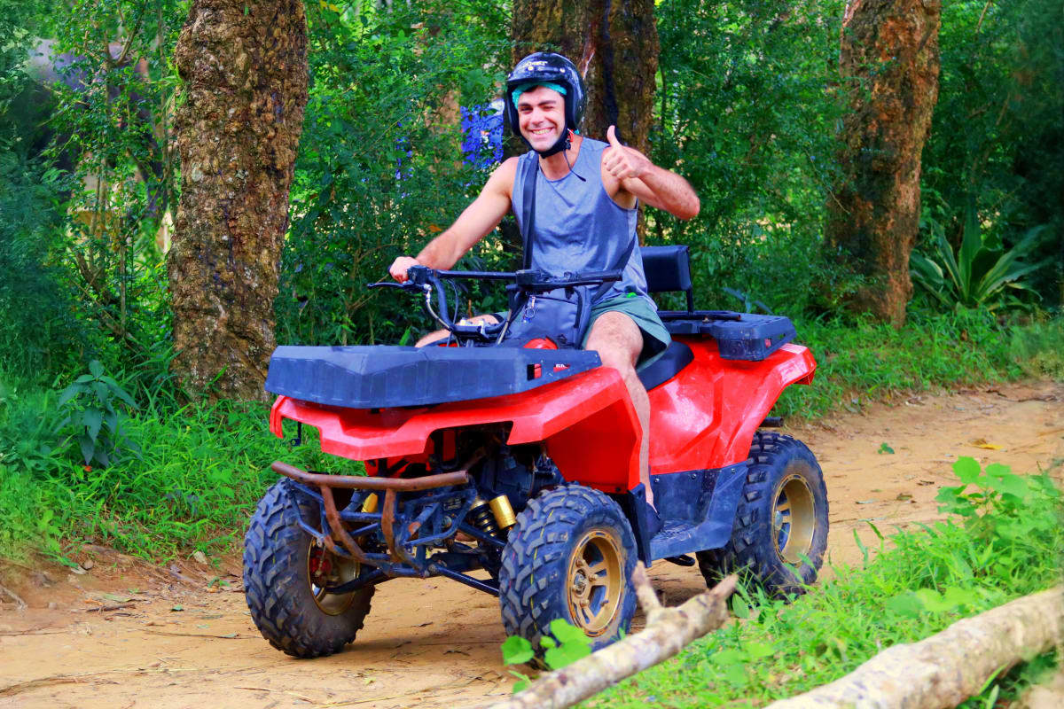 ATV and Buggy Man riding red ATV on forest trail giving thumbs up while wearing helmet