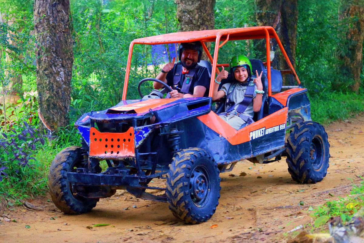 Man and woman riding orange and blue ATV buggy on jungle dirt trail surrounded by green trees in Phuket Adventure Park