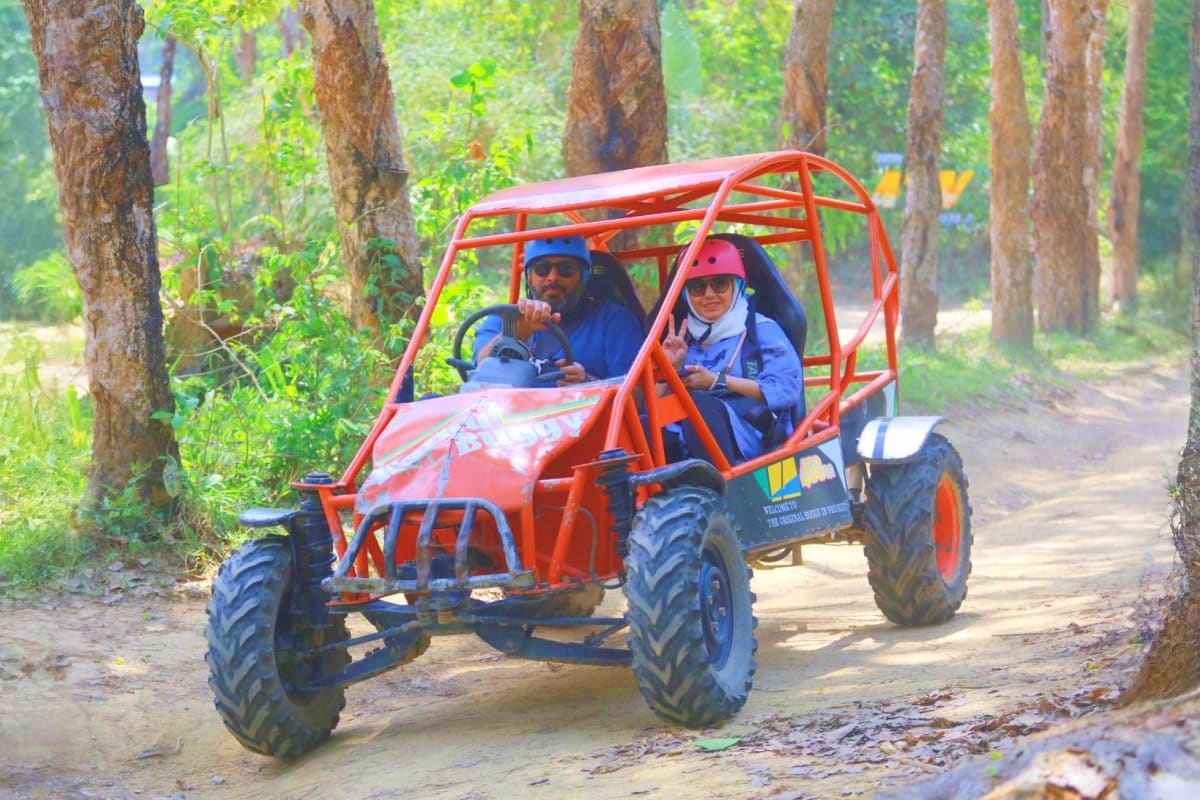 Two people riding a red buggy on a dirt forest trail surrounded by tall trees