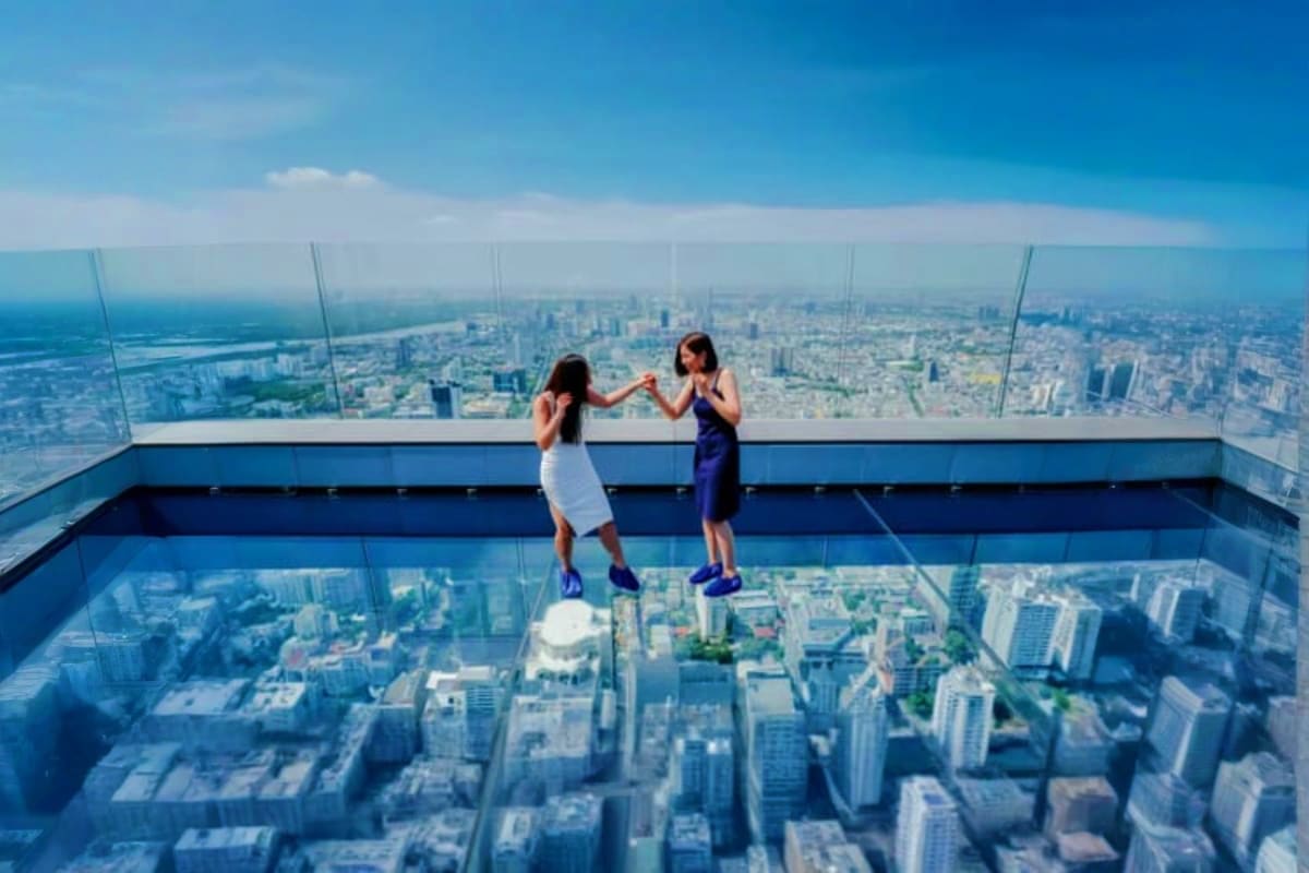 Skywalk Mahanakhon Two women holding hands on transparent glass floor of Skywalk Mahanakhon observation deck with Bangkok cityscape below