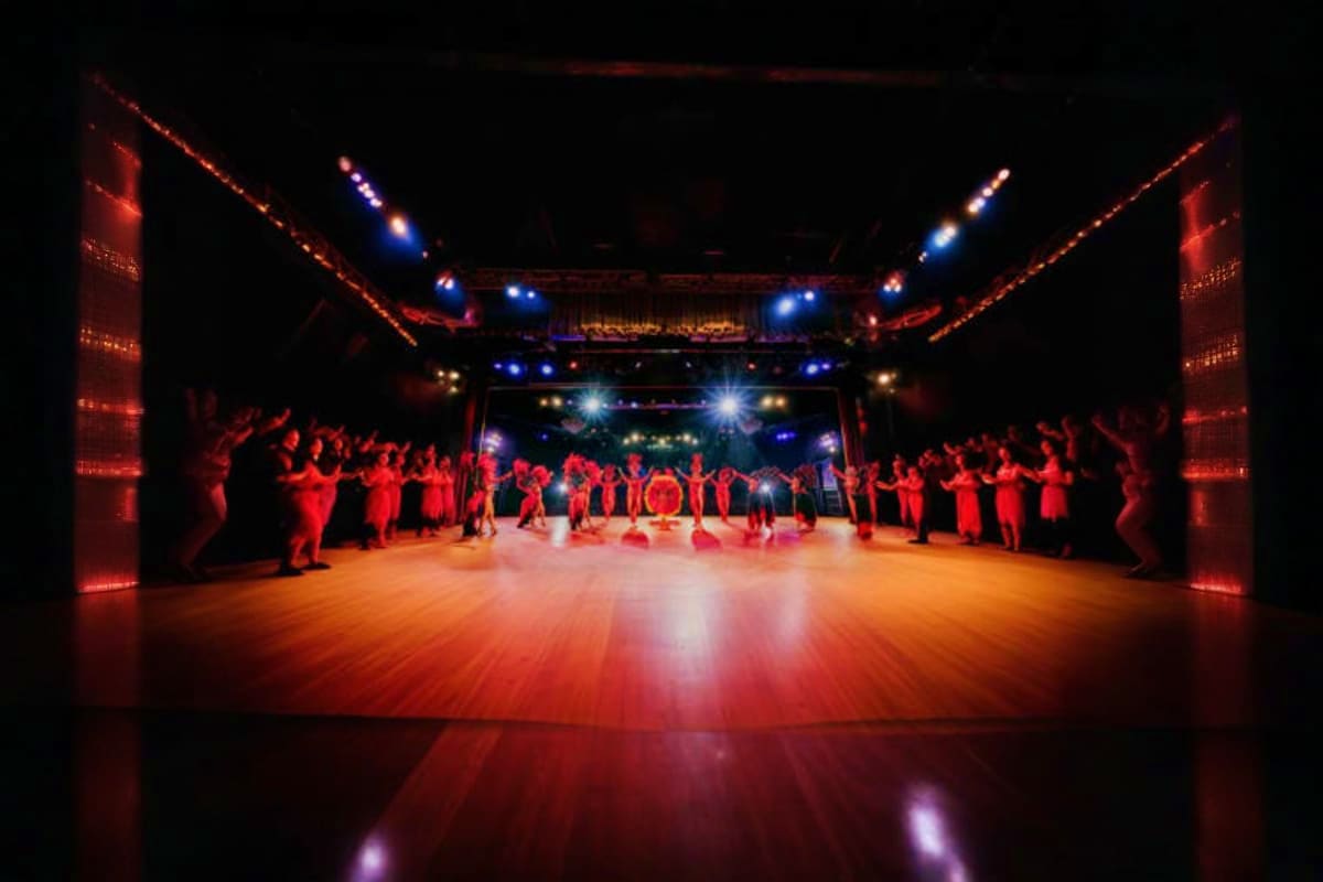 Large theater stage with wooden floor, performers in red clothing lined on both sides, professional lighting with blue and re