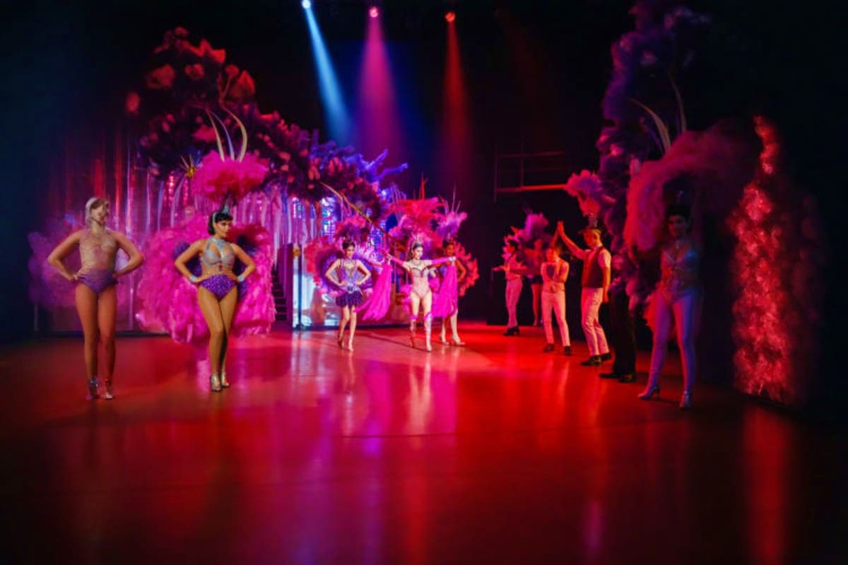 Performers on stage during Golden Dome Cabaret Show with vibrant pink and red lighting, feathered costumes, and colorful stag