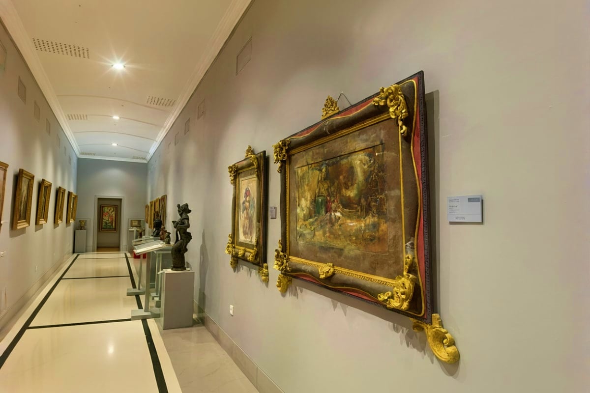 Museum Pasifika Bali Museum gallery hallway with ornate gold-framed classical paintings and sculptural displays on white walls with recessed light