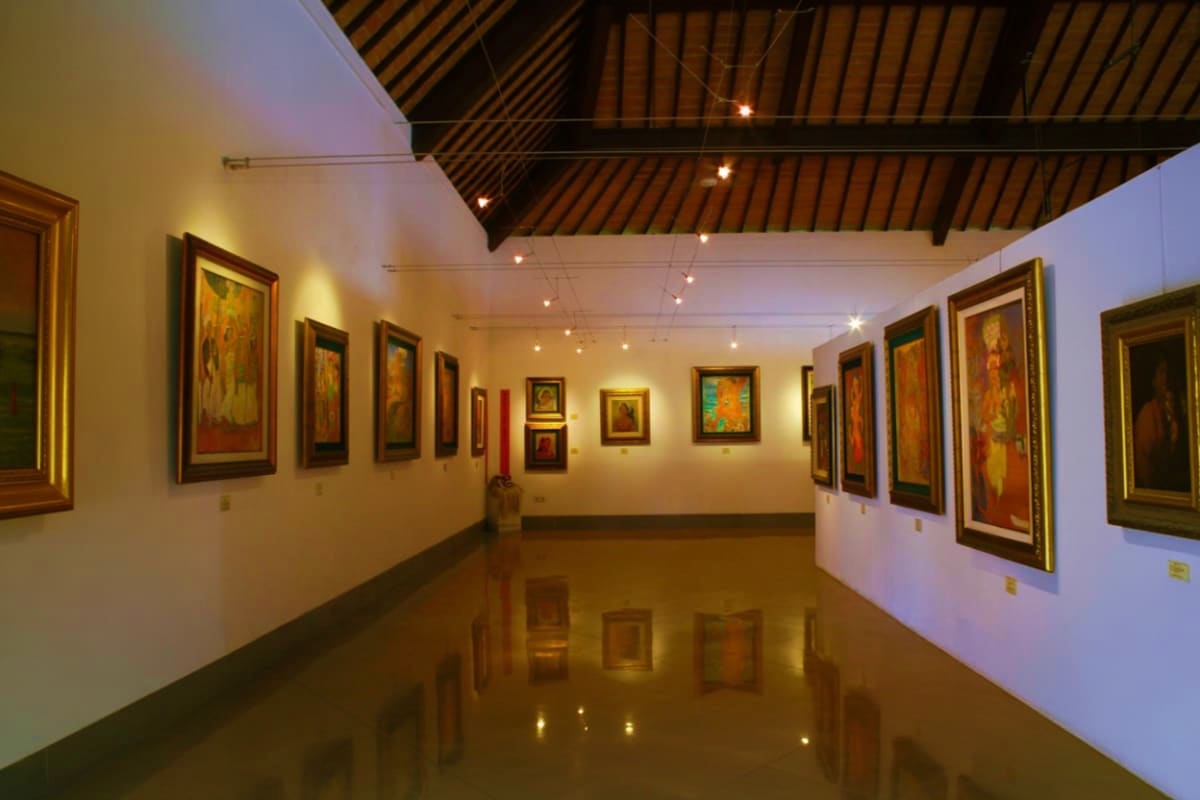 Museum Pasifika Bali Museum Pasifika Bali gallery interior with framed paintings displayed on white walls, polished floor, and wooden ceiling with