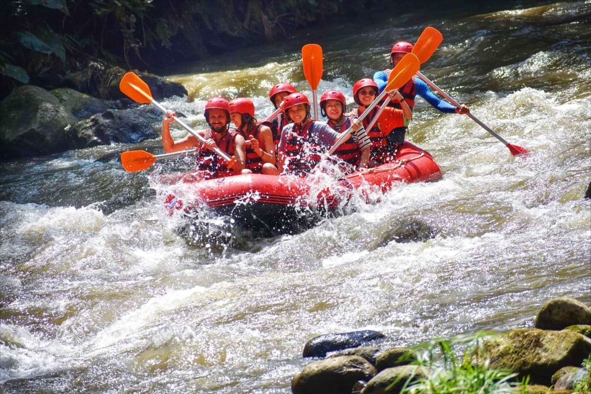 Group of people white water rafting on the Ayung River in red inflatable raft with orange paddles through whitewater rapids