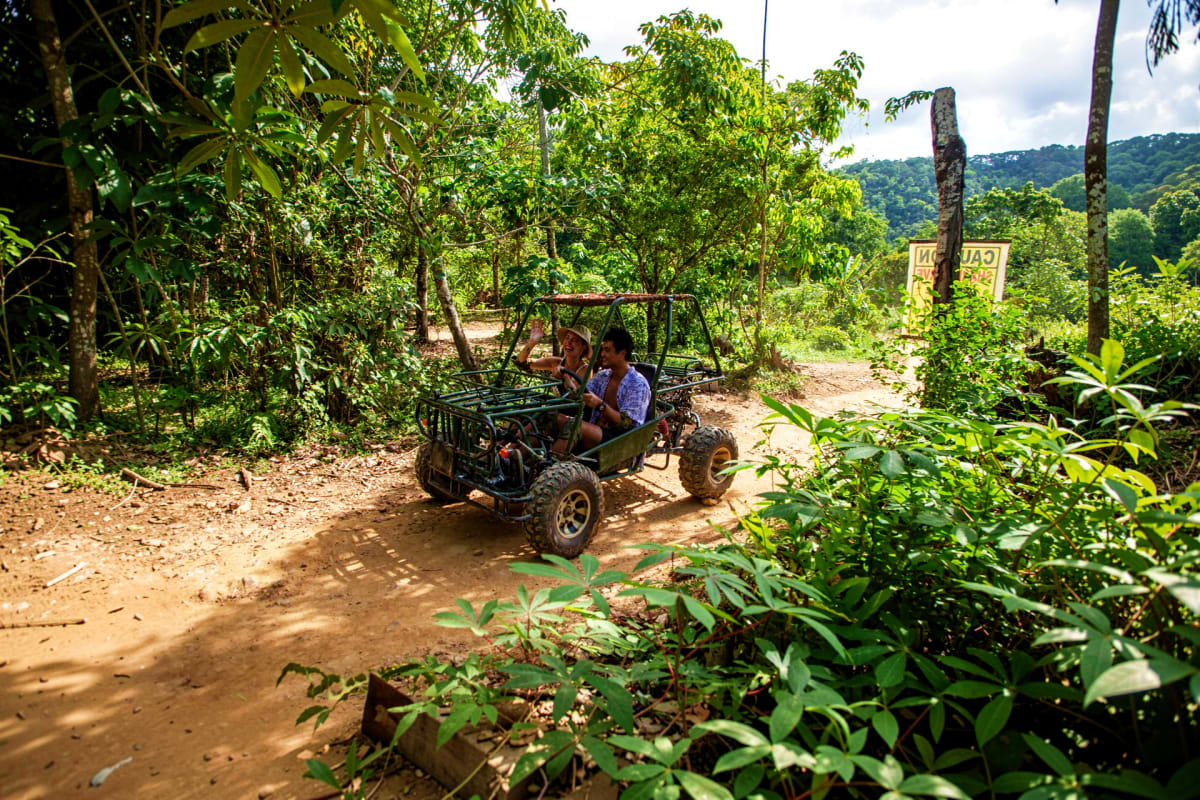 Boracay ATV and Buggy Car Adventure Two people riding an ATV buggy through a lush jungle trail surrounded by dense green vegetation and trees