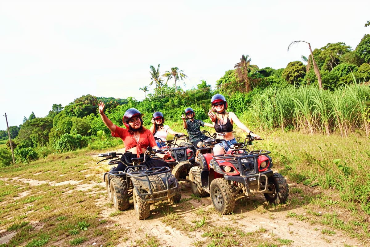 Boracay ATV and Buggy Car Adventure Group of tourists riding ATVs on muddy trail through tropical jungle landscape with palm trees and vegetation