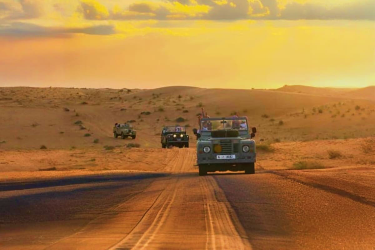 Balloon Flights with vintage car ride Vintage Land Rover vehicles driving on a desert road at sunset in the Sahara with golden sand dunes and cloudy sky
