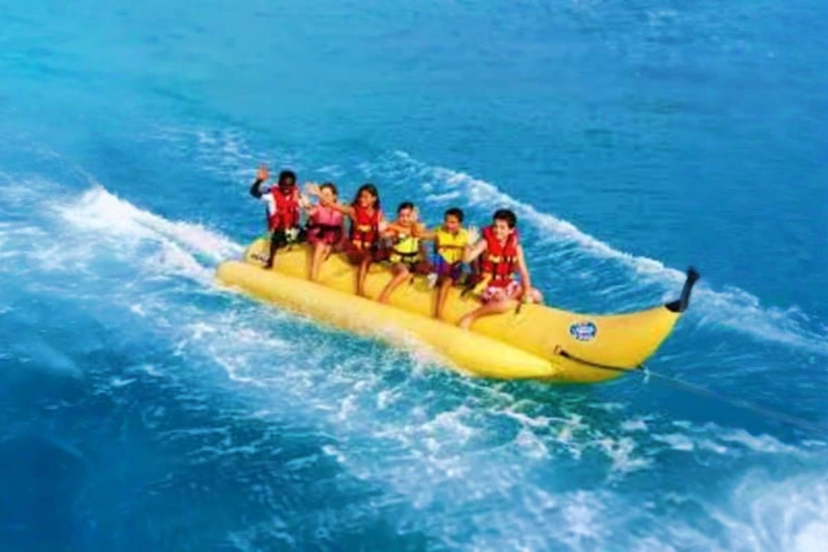 Banana Boat Ride in Dubai 15 Min Group of people riding a yellow banana boat in blue ocean waves with white caps during water sports activity