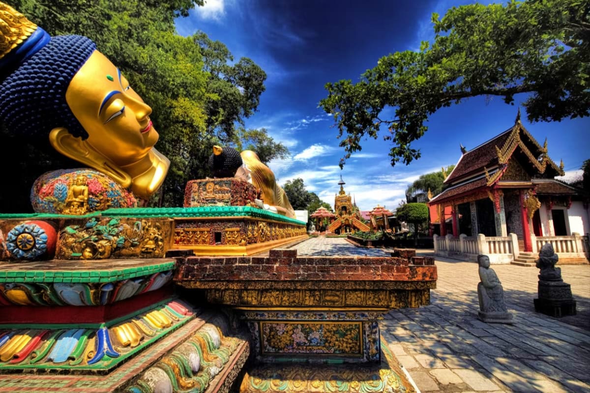 Giant golden Buddha statue at Doi Suthep Temple courtyard with ornate decorative base, traditional Thai temple buildings, and