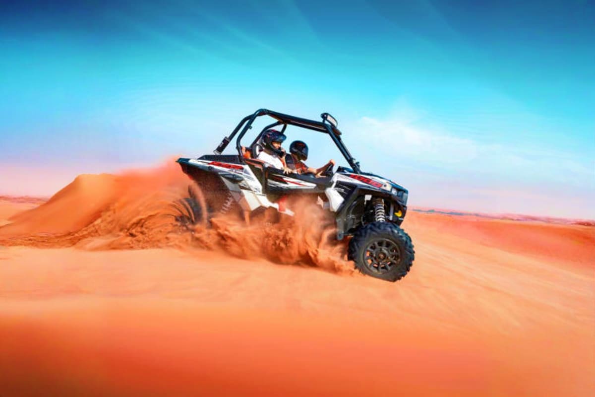 Group of tourists posing with yellow and black dune buggies on orange sand dunes under blue sky in Dubai desert (2)