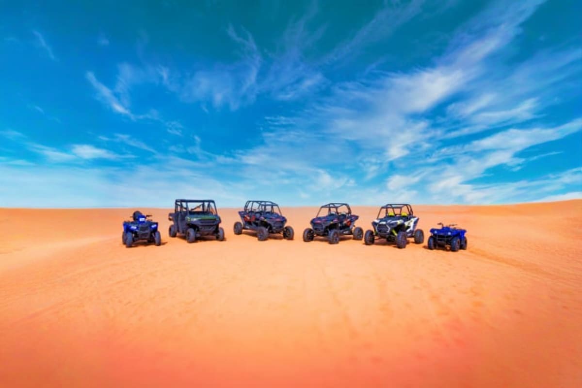 Group of tourists posing with yellow and black dune buggies on orange sand dunes under blue sky in Dubai desert (4)